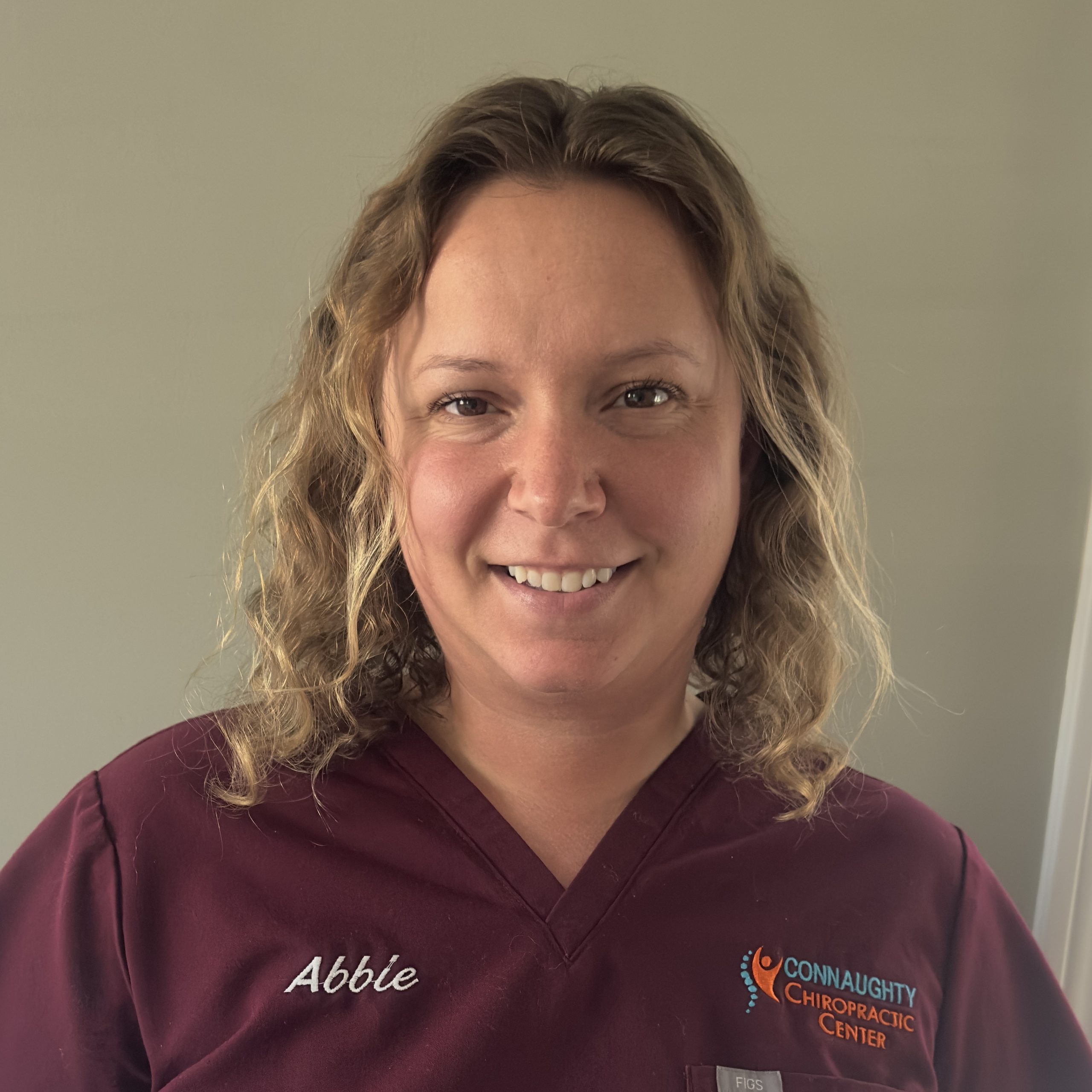 Chiropractic Old Saybrook CT Abbie Abbie standing in front of a tan wall in maroon scrubs smiling